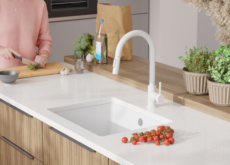 Küchenszene mit Spüle, Armatur, Lebensmitteln und einer Person, die Kräuter schneidet