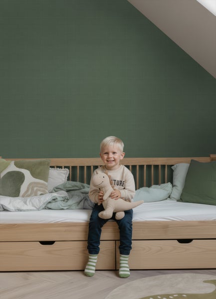 Kinderbett aus Holz mit Schubladen vor einer dunkelgrünen Strukturtapete in einem Kinderzimmer mit hellem Fischgrät-Parkett.