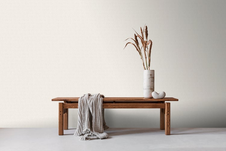 Szene mit einer Holzbank, einer Vase mit getrockneten Blumen, einer Dekofigur und einer Decke.