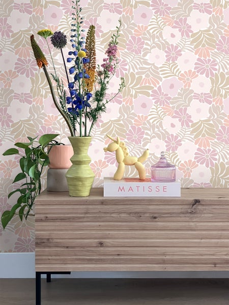 Dekorative Tapete mit Blumenmuster, kombiniert mit Kommode, Blumen und dekorativen Gegenständen für eine stilvolle Raumgestaltung.