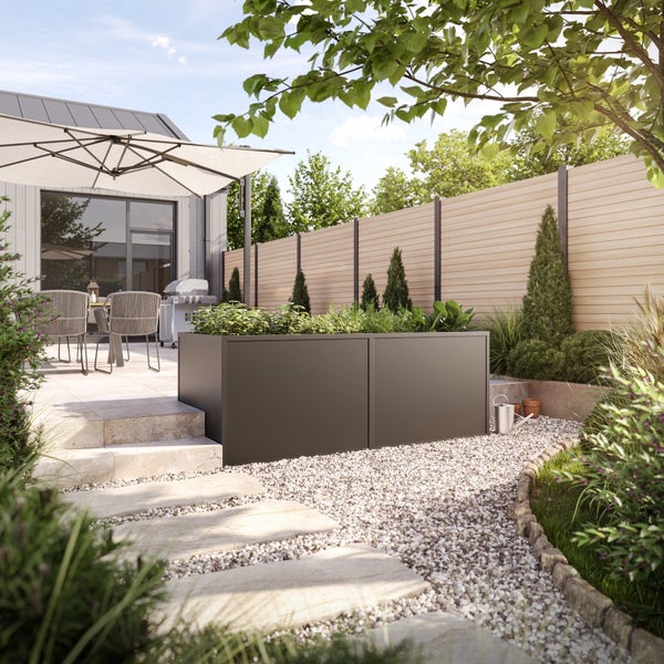 Modernes anthrazitfarbenes Hochbeet aus Metall in einem organisierten Garten mit Steinterrasse, Kiesweg und Sichtschutzzaun aus Holz.