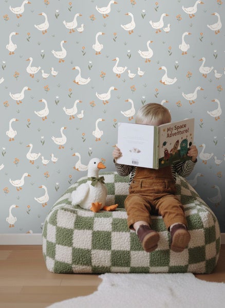 Kinderzimmer mit Gänsedesign Tapete, Kind liest Buch auf einem karierten Sessel