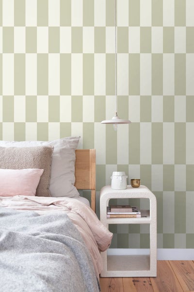 Vliestapete mit großem geometrischem Muster aus Rechtecken in Salbeigrün und Cremeweiß in einem hellen Schlafzimmer mit Bett und Nachttisch.