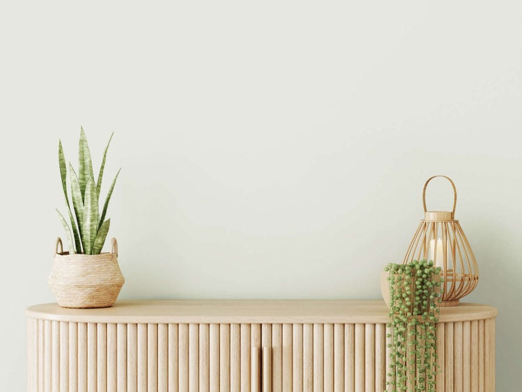 Modernes Sideboard aus hellem Holz mit vertikalen Lamellen, dekoriert mit Zimmerpflanzen und einer Holzlaterne; minimalistisch und ordentlich.
