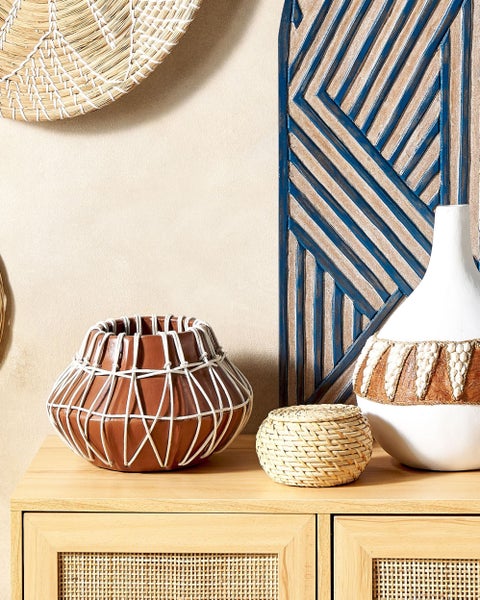 Dekorative Anordnung mit brauner Keramikvase, Strohschatulle und weißer Vase auf einer Kommode