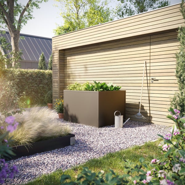 Modernes dunkelbraunes Hochbeet aus Metall in einem hellen Garten mit Kiesweg, Holzgartenhaus, Gießkanne und Rechen.