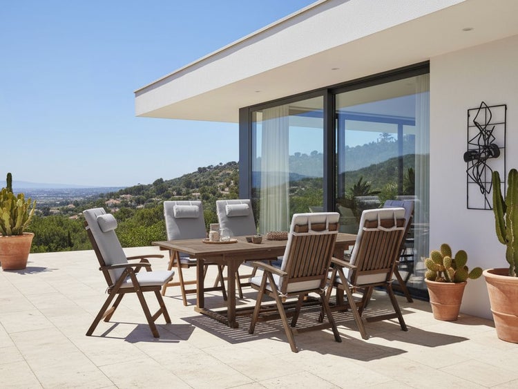 Gartenszene mit Holztisch und Stühlen mit Polsterauflagen auf einer Terrasse.