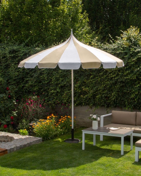 Gestreifter Sonnenschirm in Beige und Weiß mit gewelltem Rand in einem hellen Garten mit Gartenmöbeln und Blumenbeeten.