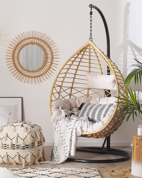 Hängesessel aus Rattan mit Kissen, Spiegel, Pouf und Teppich in einem hellen Raum.