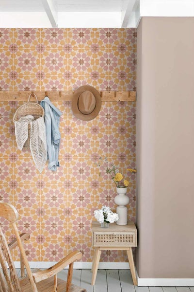 Vliestapete mit gelb-rosa Fliesenmuster, kombiniert mit einer Holzgarderobe, einem Beistelltisch aus Holz und hellen Wohnaccessoires.