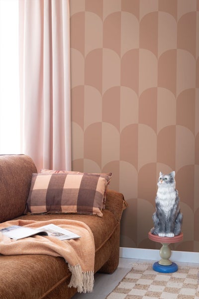 Wohnzimmer mit Vliestapete im grafischen Bogendesign, kombiniert mit einem texturierten Sofa, Kissen und einer dekorativen Katzenfigur.