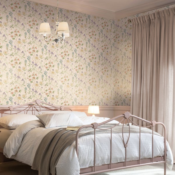 Schlafzimmer mit blumiger Tapete, Metallbett und Vorhängen in einer gemütlichen und hellen Einrichtung.
