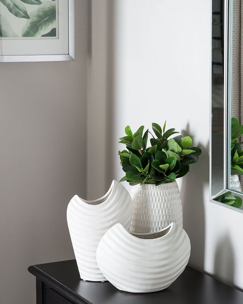 Dekorative weiße Keramikvasen und Kunstpflanzen auf einem Schrank