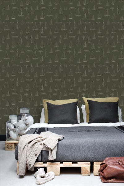 Tapete mit Segelschiff-Muster in einem Schlafzimmer mit Palettenbett, grauer Decke und dunklen Kissen.