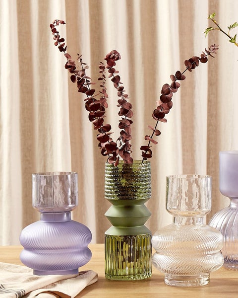 Dekorative Glasvasen in verschiedenen Ausführungen und Farben auf einem Tisch mit Zweigen