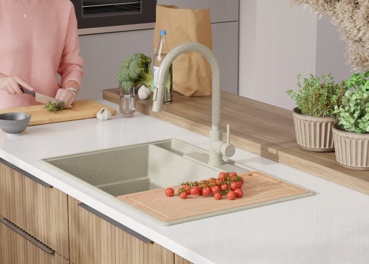 Küchenszene mit Spüle, Armatur, Schneidebrett und Lebensmitteln auf einer Küchentheke.