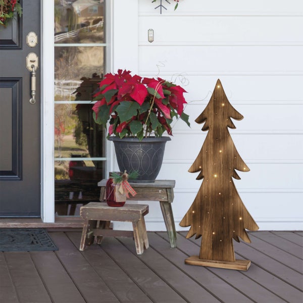 Dekoratives Holzweihnachtsbaumornament mit Beleuchtung auf einer Veranda neben Topfpflanze und Dekoration