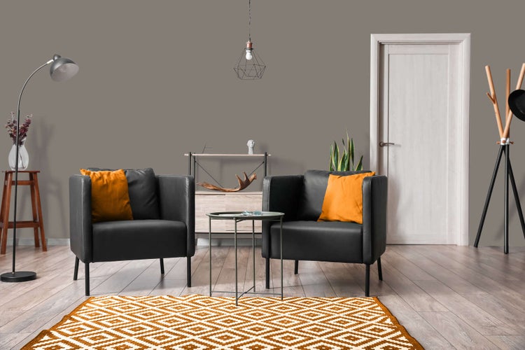 Modernes Wohnzimmer mit grauer Wandfarbe, zwei schwarzen Sesseln, orangefarbenem Teppich und hellem Laminatboden.