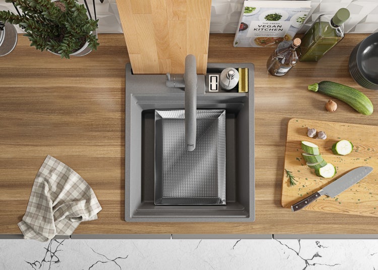 Küchenspüle mit Abtropfschale und Armatur auf einer Arbeitsplatte mit Lebensmitteln und Utensilien.