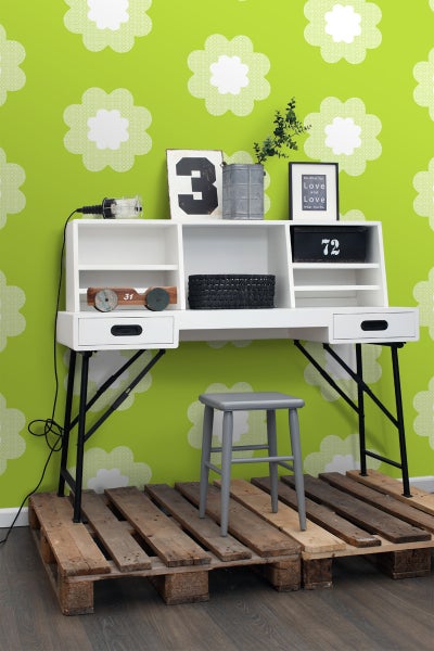 Schreibtisch mit Regalen und Schubladen auf einer Holzpalette mit einem Hocker vor einer Wand mit Blumendesign.