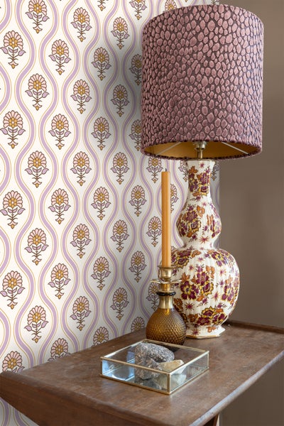 Dekoratives Interieur mit gemusterter Tapete, Tischleuchte, Kerze und Dekorationen auf einem Holztisch