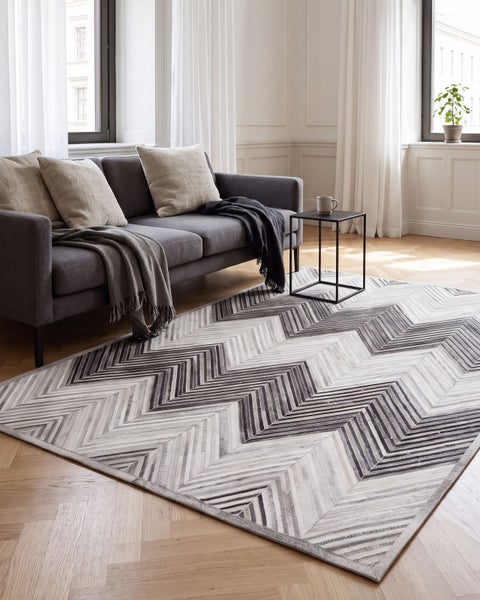 Wohnzimmer mit einem großen Teppich mit Zickzack Muster in einem hellen, modern eingerichteten Raum mit Sofa und Beistelltisch.