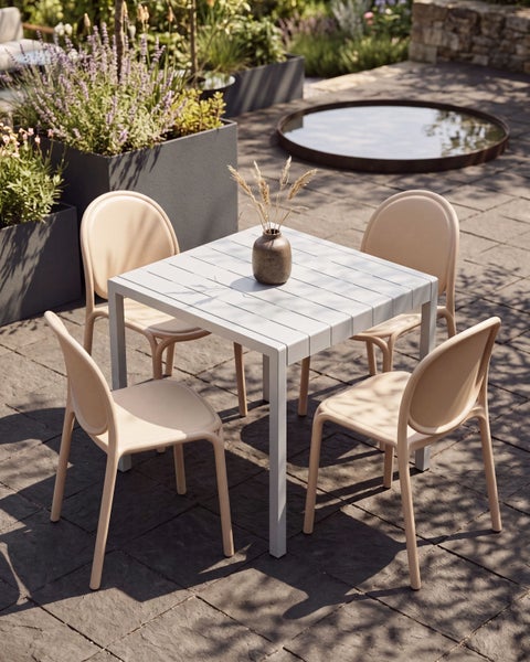 Moderne Gartengruppe mit quadratischem, grauem Tisch und vier beigen Stühlen auf einer gepflasterten Terrasse mit Pflanzkübeln.