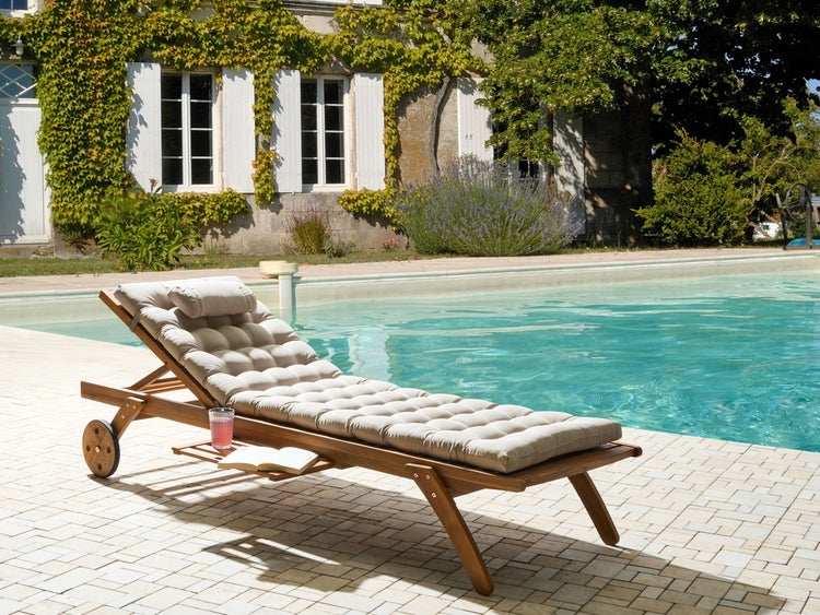 Szene mit einer Holzliege mit Auflage und einem Getränk am Pool