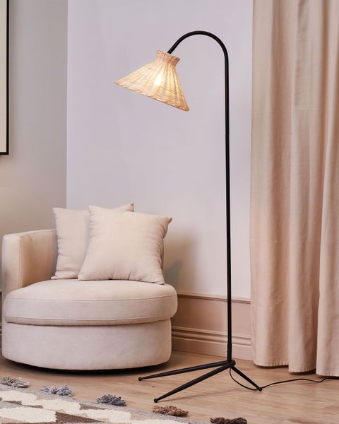 Stehlampe mit Lampenschirm aus Rattan neben Sessel und Vorhang
