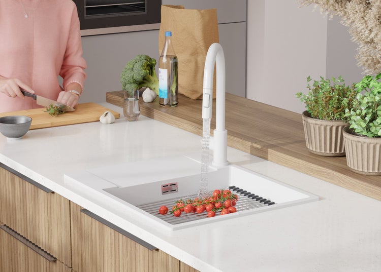 Küchenszene mit Spüle, Armatur und Gemüse. Person schneidet Kräuter auf einem Schneidebrett.