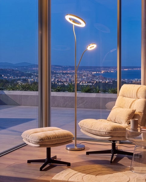 Moderne LED Stehleuchte mit zwei verstellbaren Lichtringen neben einem Polstersessel mit Hocker vor einer großen Fensterfront mit Stadtblick