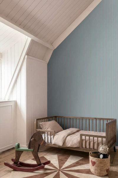 Ein Kinderzimmer mit einer Tapete mit vertikalem Streifenmuster, einem Holzbett, einem Schaukelpferd aus Holz und einem runden Teppich.