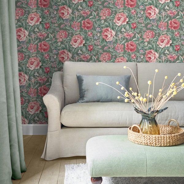 Wohnzimmer mit Vliestapete mit Rosenmuster, gepolstertem Sofa, Hocker und dekorativer Blumenvase in einer gemütlichen Wohnumgebung.