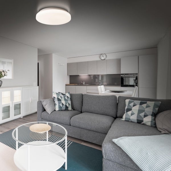 Helles Wohnzimmer mit grauer Eckcouch, Glascouchtisch und Deckenleuchte