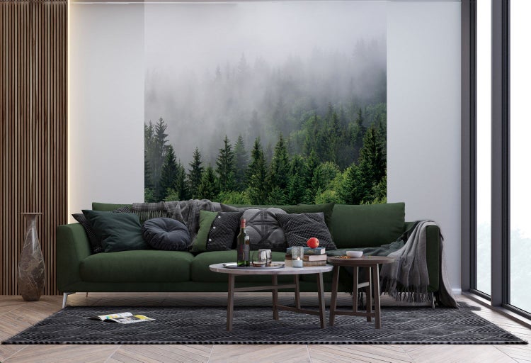 Wohnzimmer mit grünem Sofa, Couchtischen und Waldtapete für eine naturverbundene Atmosphäre.