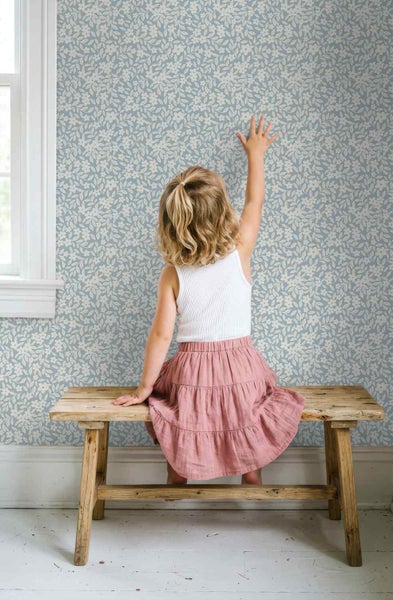 Blumentapete mit weißem Blüten- und Blattmuster in einem hellen Kinderzimmer mit einer Holzbank.