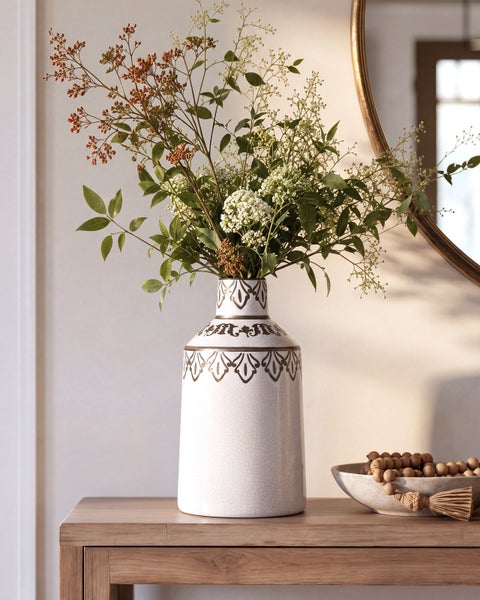 Dekorative Keramikvase mit Rissoptik und floralem Muster, gefüllt mit einem Strauß aus Ästen und Blüten auf einem Holztisch.