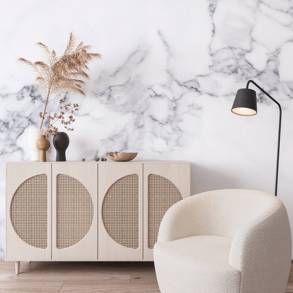 Fototapete in Marmor-Optik in einem Wohnzimmer mit hellem Sideboard mit Wiener Geflecht, einem runden Sessel und einer schwarzen Stehlampe.