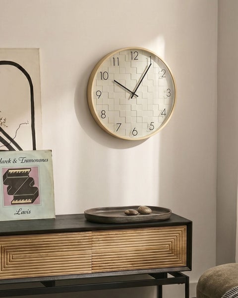 Runde Wanduhr mit Holzrahmen und strukturiertem Zifferblatt an einer Wohnzimmerwand über einer Kommode.