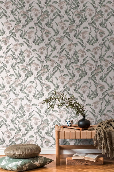 Wohnraum mit floral gemusterter Tapete, Sofa, Kissen, Decke, Bücherstapel und Tischlampe