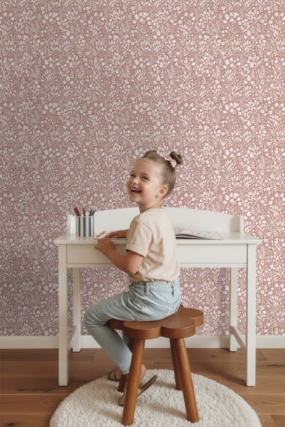 Mädchen am Schreibtisch vor Wandtapete mit floralem Muster