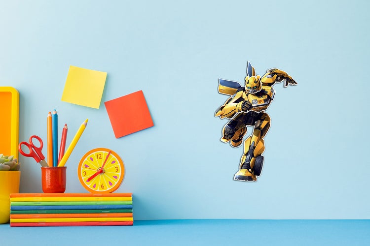 Wandtattoo Transformers Bumblebee in einem Kinderzimmer über einem Schreibtisch mit Heften, Stiften und einer Uhr.