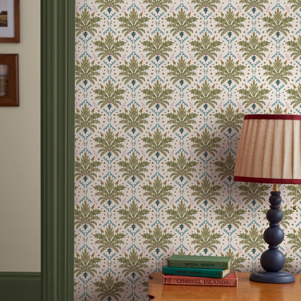 Vliestapete mit botanischem Ornament-Muster an einer Wand neben einer Tischleuchte und Büchern.