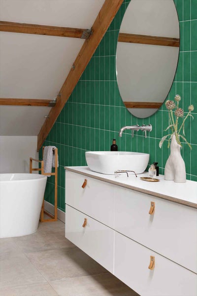 Modernes Badezimmer mit Waschtisch und runden Spiegel vor einer Wand mit grünen Fliesen im Dachgeschoss.