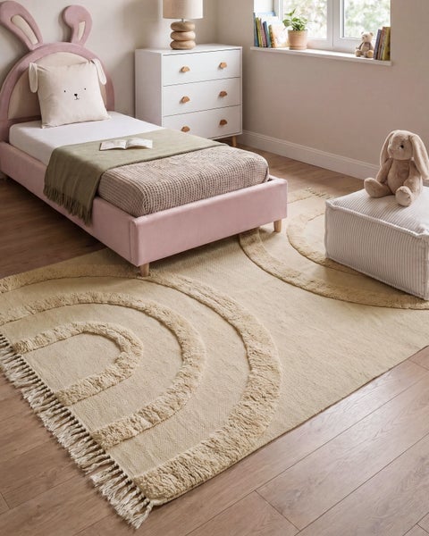 Beiger Kinderzimmer Teppich mit strukturiertem Regenbogenmuster und Fransen in einem modern eingerichteten Kinderzimmer.