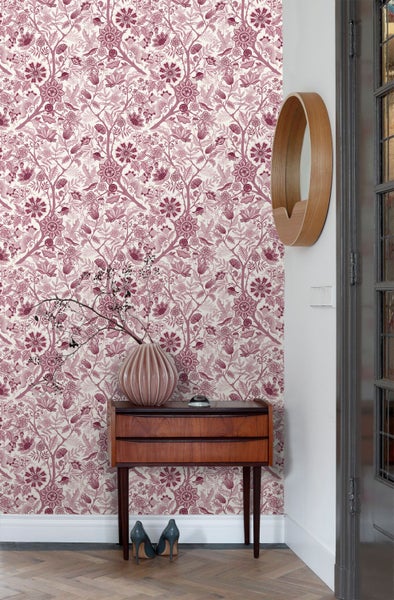 Hell gestalteter Raum mit floraler Mustertapete, hölzernem Sideboard, einer Vase und Fischgrätparkett.