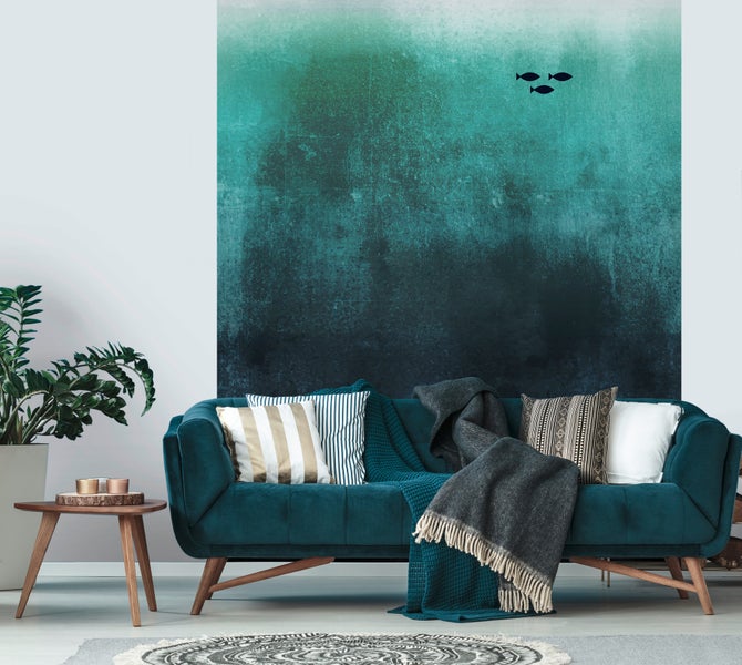 Wohnzimmer mit dunkeltürkisem Samtsofa, dekorativen Kissen und einer Wandfototapete mit Farbverlauf und Fischmotiven.