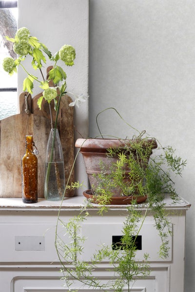 Dekorative Stillleben-Szene mit Pflanzen, Vasen und Holzschneidebrettern auf einem weißen Schrank.