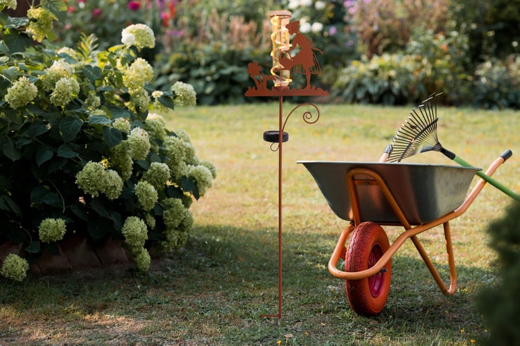 Szene im Garten mit Schubkarre, Rechen und Solar-Regenmesser.