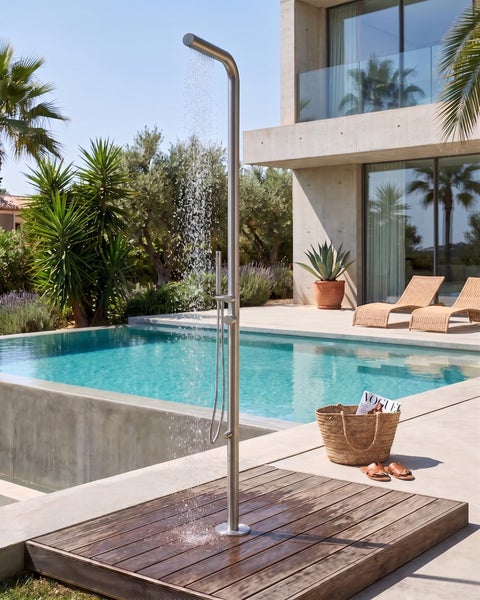 Freistehende Außendusche aus Edelstahl an einem Pool mit Holzpodest in einem modernen, hellen Garten.